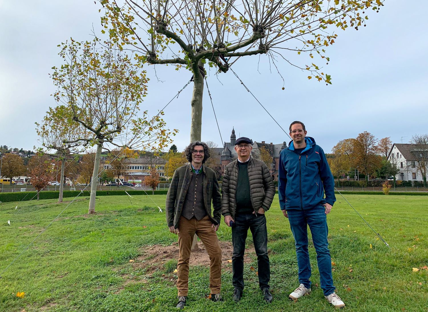 Drei Männer stehen vor Bäumen in einem Sportpark