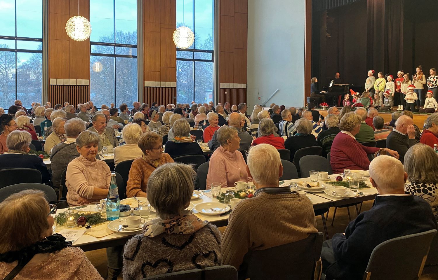 Senioren an Kaffeetafeln vor Bühne, auf der Kinder singen