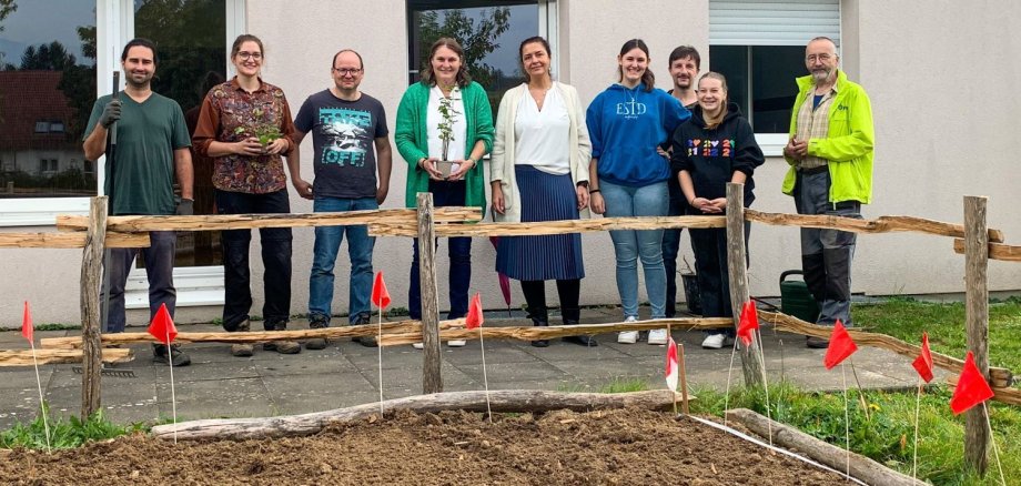 Männer und Frauen mit Spaten und Pflanzen vor Pflanzbeet