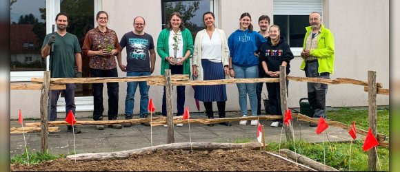 Männer und Frauen mit Spaten und Pflanzen vor Pflanzbeet