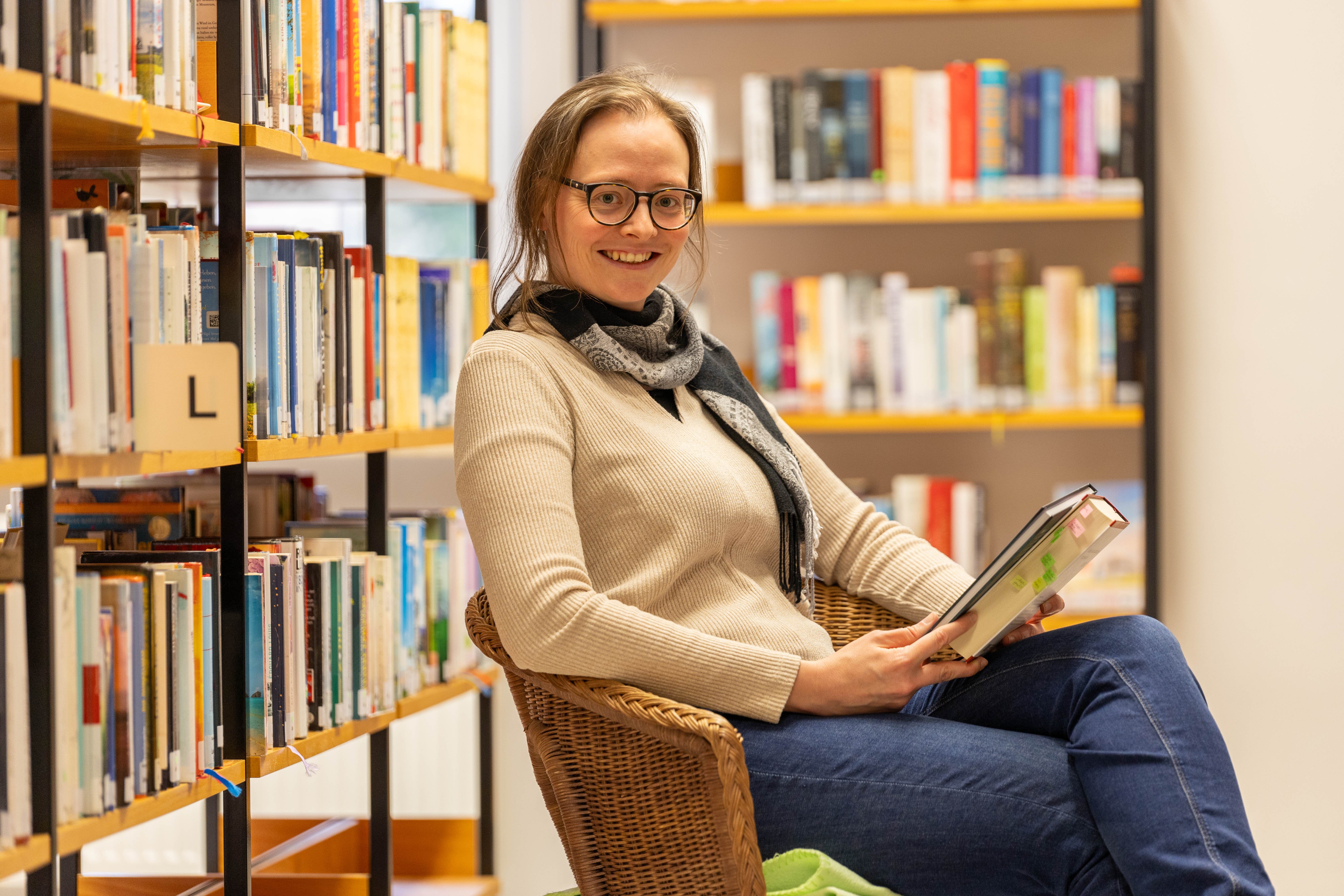Frau sitzt mit Buch in der Hand in einem Sessel 