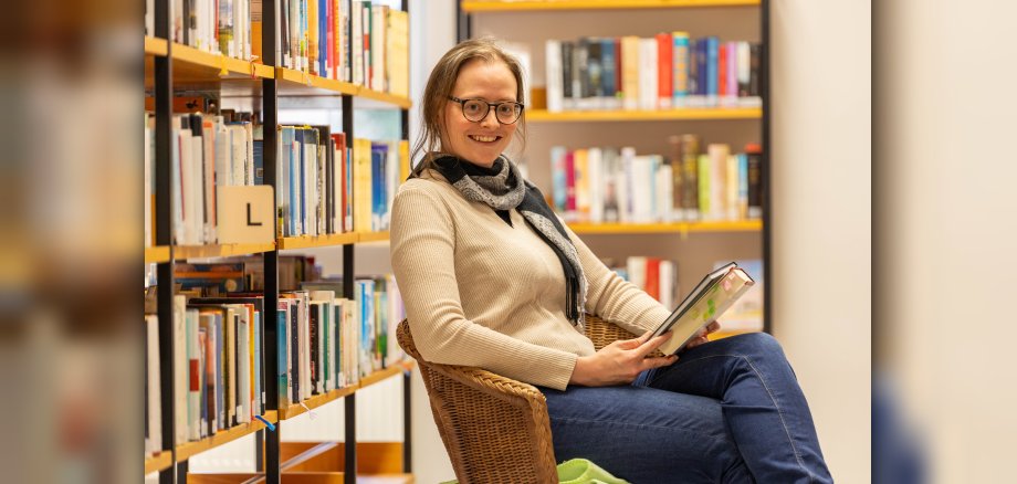 Frau sitzt mit Buch in der Hand in einem Sessel 