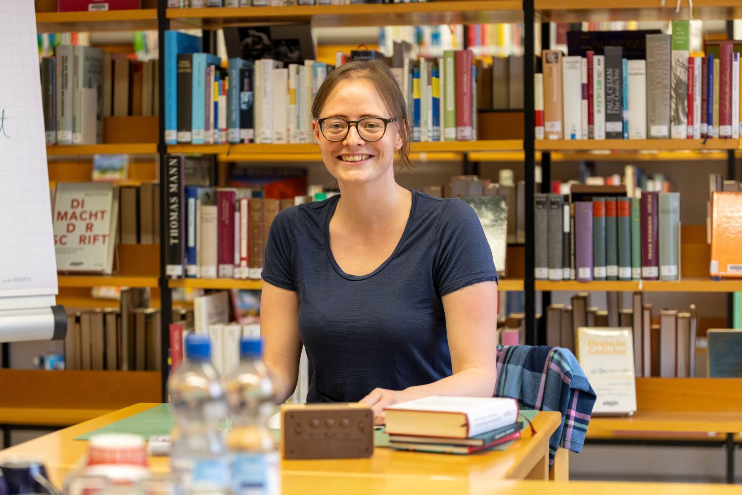 Workshopleiterin Sarah Klein Frau sitzt in Bücherei an Tisch mit Büchern vor sich