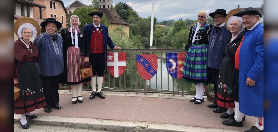 Mitglieder zweier Trachtengruppen in Tracht auf Brücke mit Wappen