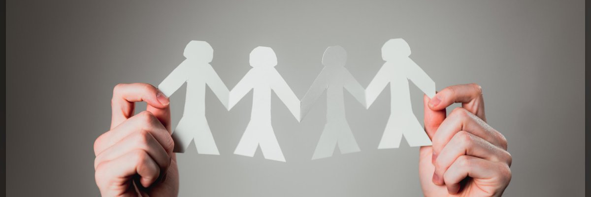 Papierfiguren als Gesellschaft Zwei Hände halten eine Girlande aus Papiermenschen hoch