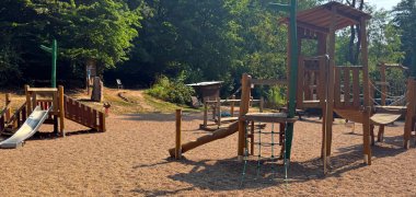Verschiedene Spielgeräte aus Holz auf einem Spielplatz im Wald.