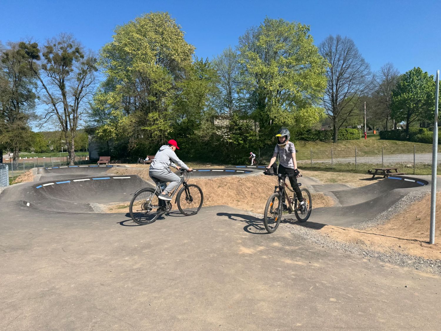 Kinder mit BMX-Bike und Roller warten darauf,  auf einer asphaltierten Pumptrack-Strecke fahren zu können.