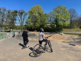 Kinder mit BMX-Bike und Roller fahren auf einer asphaltierten Pumptrack-Strecke