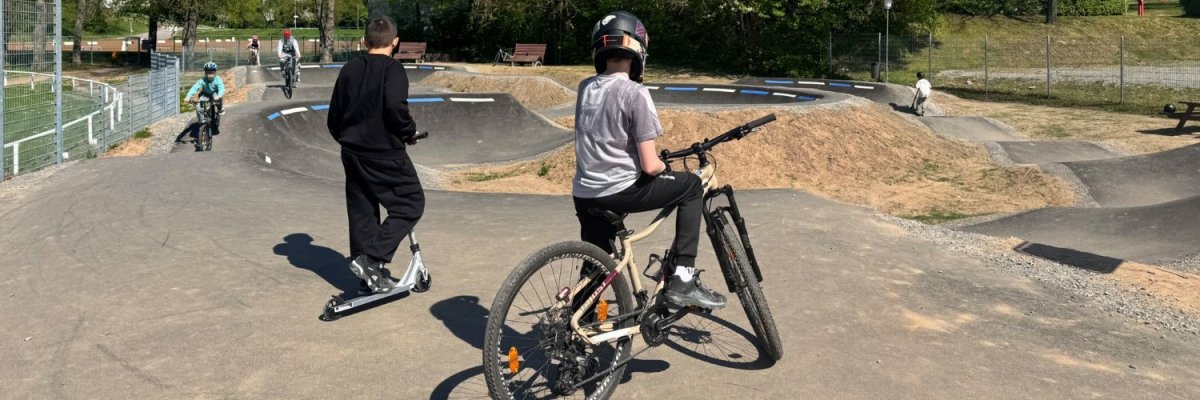 Kinder mit BMX-Bike und Roller fahren auf einer asphaltierten Pumptrack-Strecke