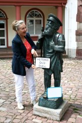 Heiteres Quizduell Frau posiert neben Statue und hält Schilder mit Aufschrift "Heiteres Quizduell"